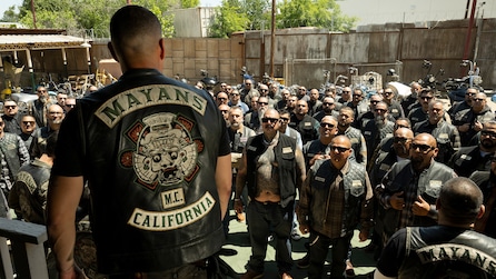 EZ facing a crowd of men, wearing a vest that reads "Mayans MC California"