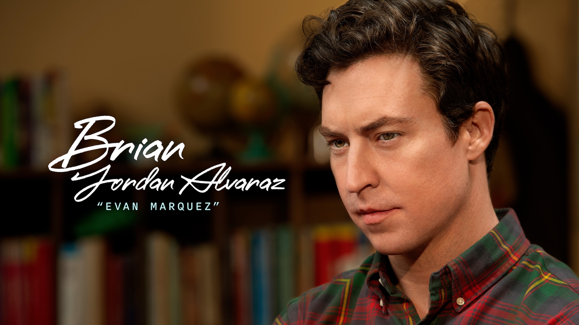 Brian Jordan Alvarez as Evan Marquez in FX's English Teacher, wearing a plaid button up with a bookshelf behind him.