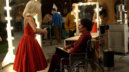 Jessica Lange as Joan Crawford sitting in wheelchair backstage talking to woman in red dress in Feud FX show