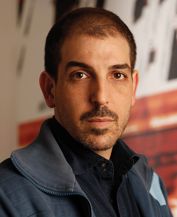 Glenn Kessler headshot in blue jacket and blue button down with red and white graphic image background