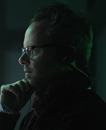 Noah Hawley headshot of his side profile, wearing glasses and placing his hand on his chin