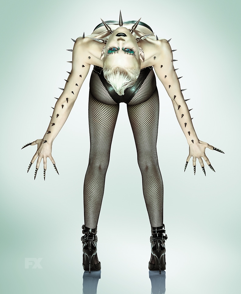 Person in black heels and fishnet tights bending backwards with arms out with spikes from FX'S AHS NYC