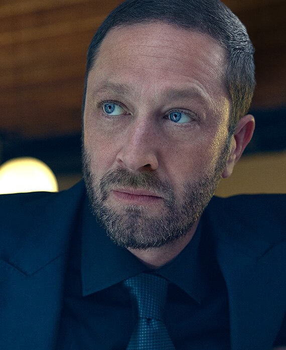 Ebon Moss-Bachrach headshot wearing a navy suit and tie.