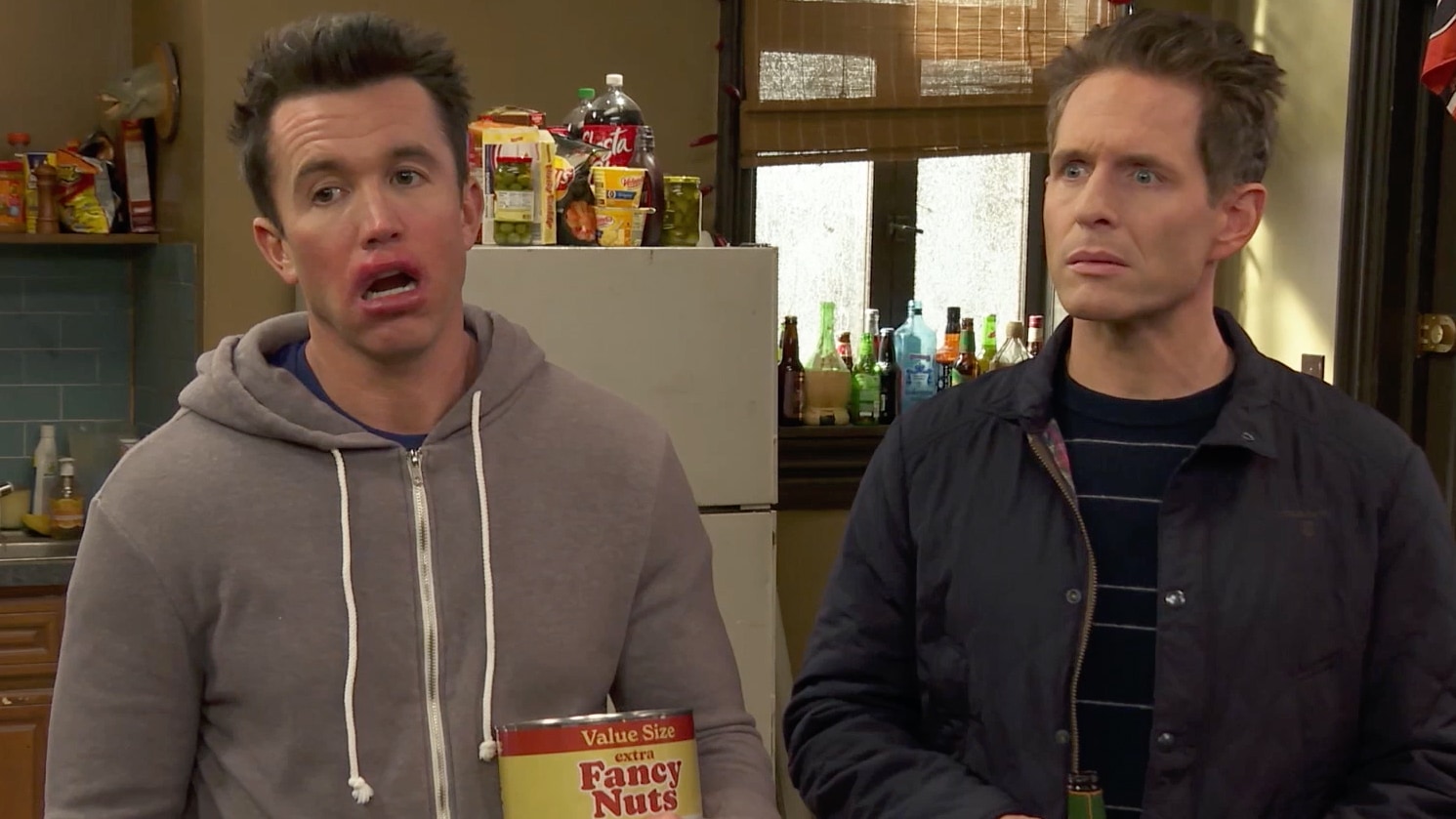 Mac holding a tin of nuts next to Dennis, standing in the kitchen