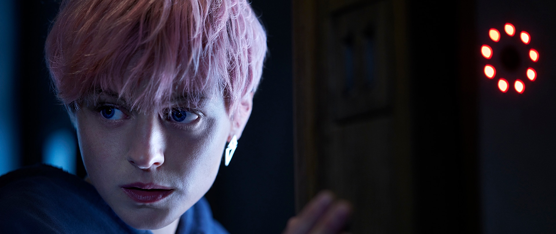 Woman with short, pink hair wearing a blue zip-up jacket.