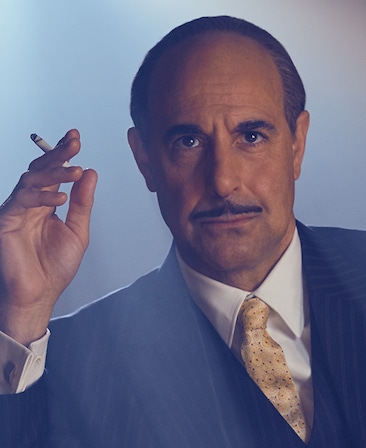 Stanley Tucci as Jack L Warner holding a cigarette wearing striped suit and gold tie for Feud FX show 
