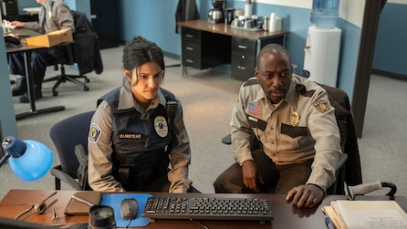 A man and woman in sheriff outfits sitting next to each other at a desk in front of a keyboard. 