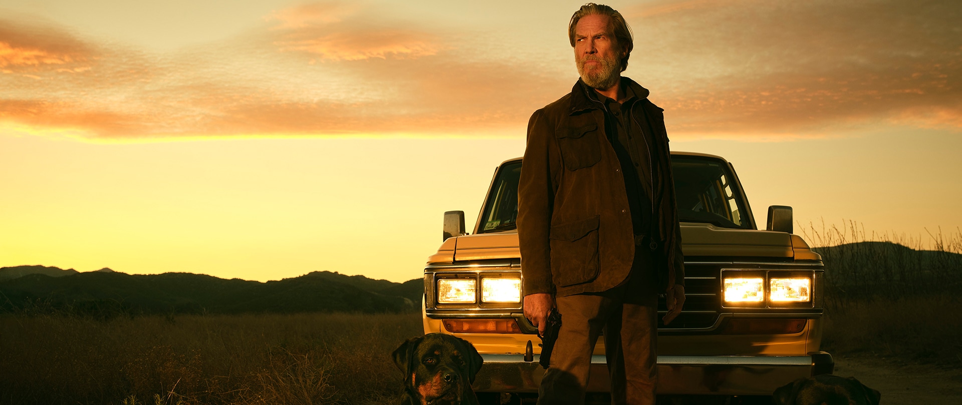 Jeff Bridges as Dan Chase, standing in front of a yellow car with two dogs, in the middle of the desert.