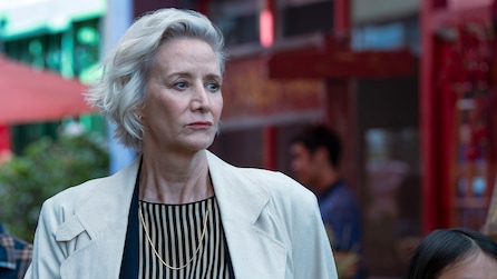 Woman with silver hair wearing a creme colored blazer and striped blouse.