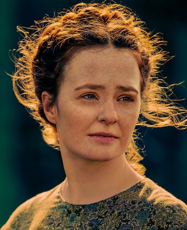 Laurie Ogden headshot in floral design top with blue and green flowers with sun brightly shining on hair up in bun