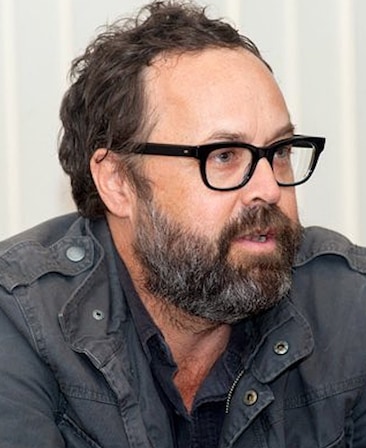Scott Robertson headshot wearing a gray cargo jacket and black glasses standing in front of a white background