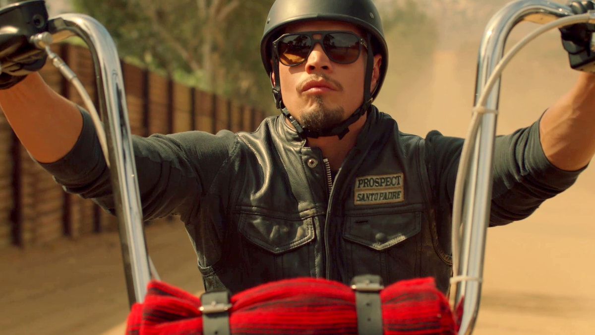 EZ wearing a leather vest and helmet while riding a motorcycle on a dirt road