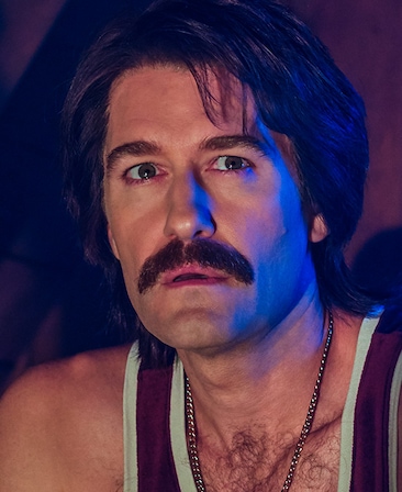 Matthew Morrison headshot with mustache in tank top and silver chain with blue light on face from American Horror Story 1984