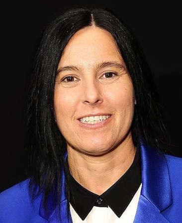 Andrea Sperling headshot wearing a blue suit jacket standing against a black backdrop