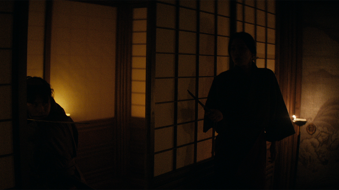 A dark silhouette of a shinobi assassin holding a dagger in a room lit by an oil lamp
