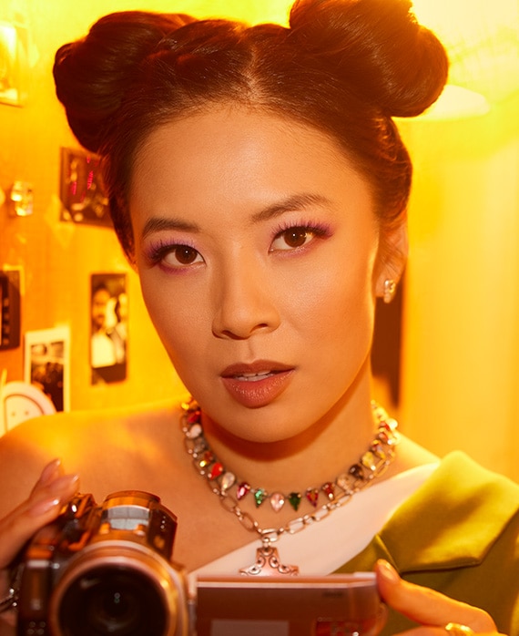 Christine Ko wearing a multi colored necklace and her hair in space buns while holding a video camera