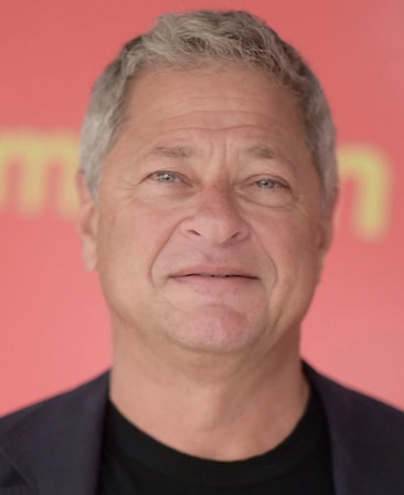 Michael Rotenberg headshot wearing a black shirt and black jacket standing in front of a red sign