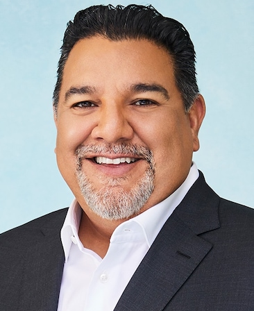 Headshot of executive producer of FX's Necaxa, Cris Abrego, wearing a white collared button down and a grey suit.