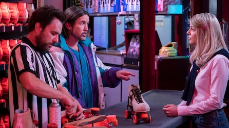 Charlie in black and white shirt screwing roller skates with Mac and talking to woman in pink in FX's It's Always Sunny