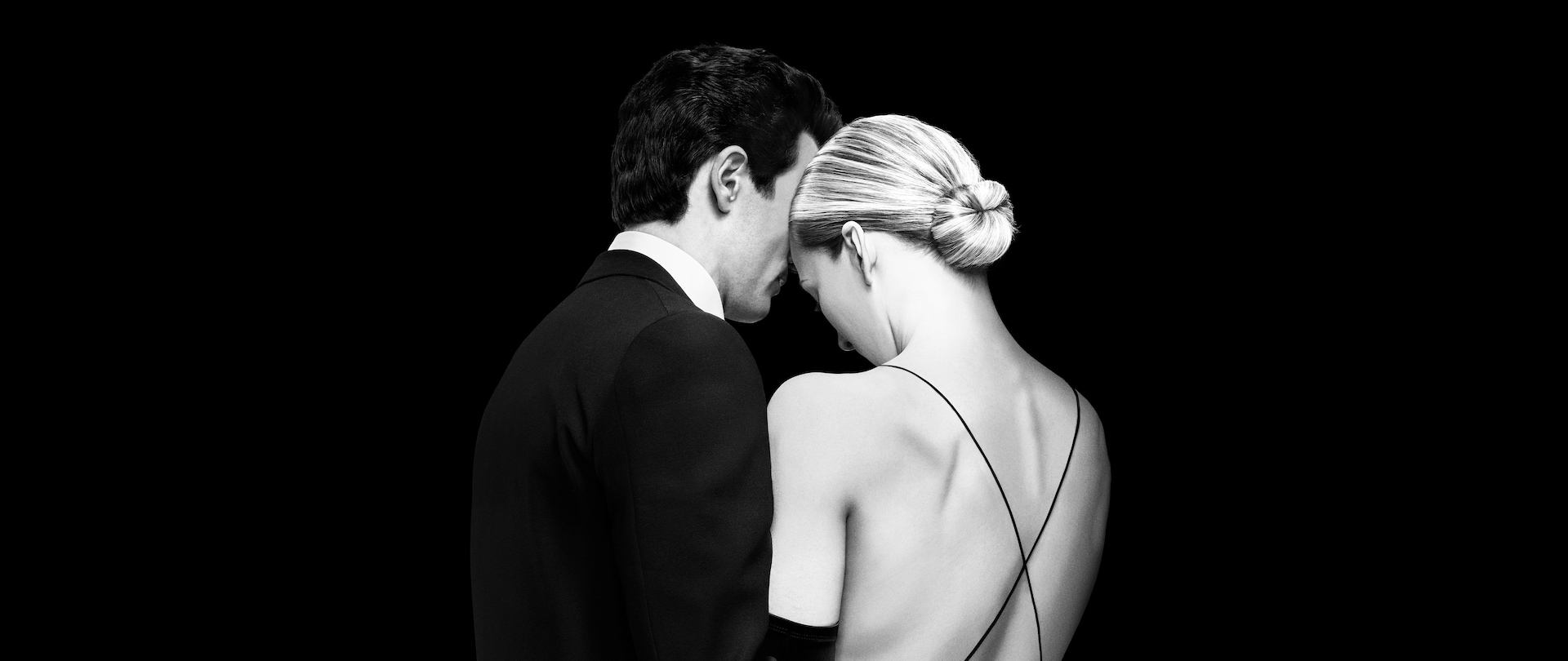Black and white portrait of the backsides of John F. Kennedy Jr and Carolyn Bessette standing close together in formal attire