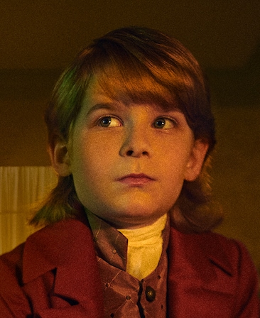 David Alexander headshot in red blazer and red satin vest with white neck tie, looking up to the side in room with white wall