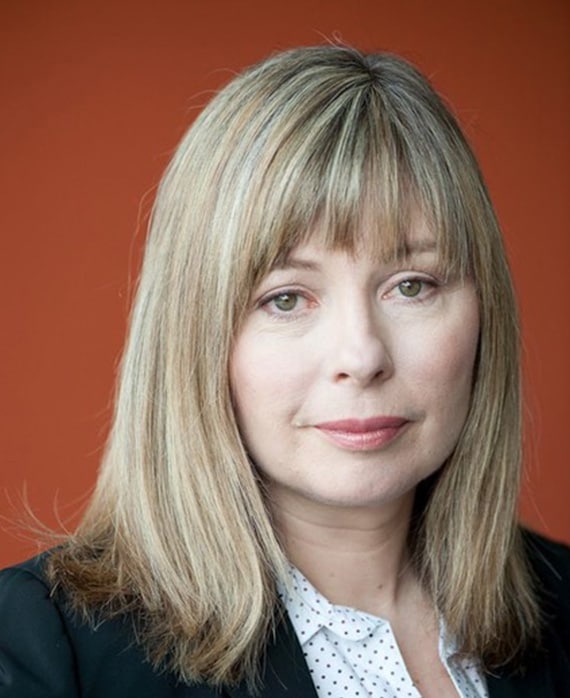 Kim Todd wearing a polka dot shirt with a black jacket, standing against a orange background