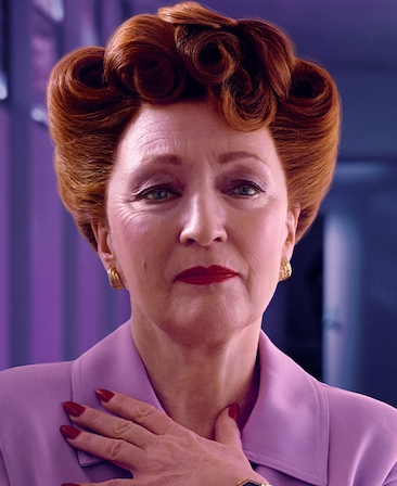 Lesley Manville as Nurse Redd in FX's Grotesquerie with her hair in an updo, wearing red lipstick in a purple coat.