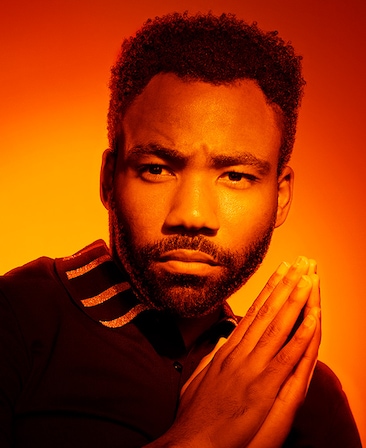 Donald Glover headshot with hands clasped together with orange sunset lighting over face and background