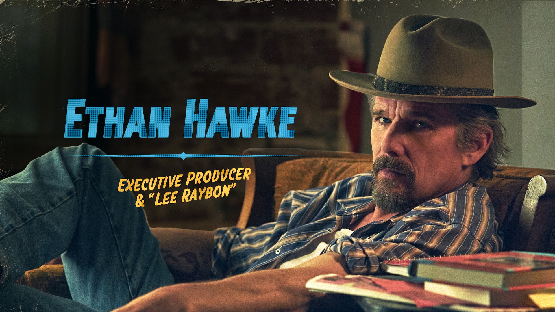 Ethan Hawke as Lee Raybon in FX's The Lowdown, wearing a striped top and tan fedora, laying back on a brown couch.