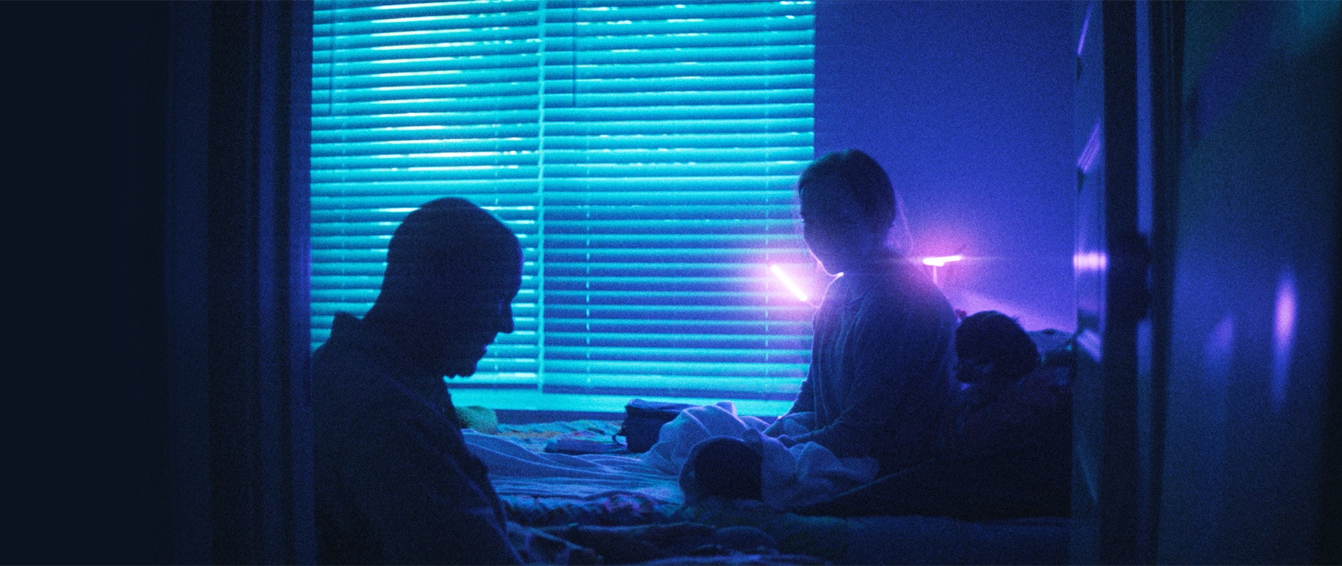 Man and woman sitting across from one another in front of blinds in a dimly lit bedroom