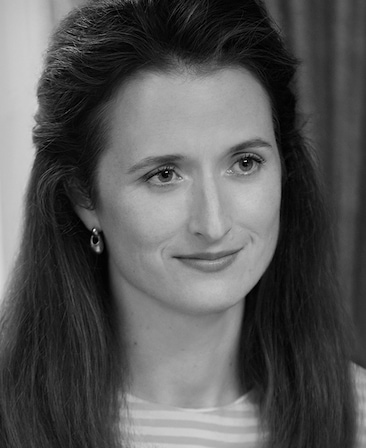Headshot of Grace Gummer as Caroline Kennedy in FX's Love Story wearing hanging earrings and a striped shirt.