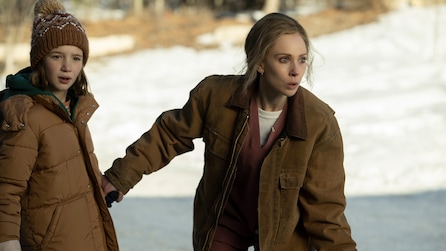 Blonde woman in brown jacket holding hands with a young girl wearing a brown beanie and coat. 