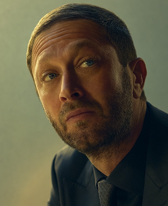 Ebon Moss-Bachrach headshot wearing a navy suit and tie.