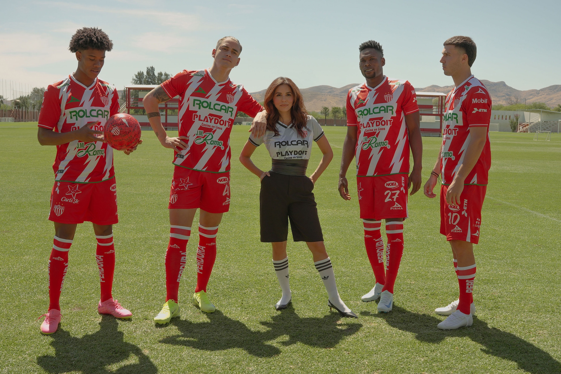 Eva Longoria standing in the center of 4 soccer players on a field.