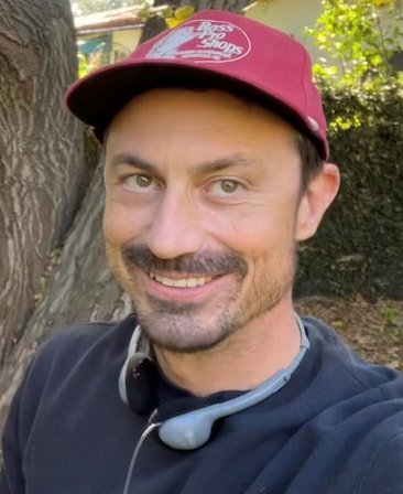 Executive producer and Writer Rob Rosell, wearing navy blue crew neck and a red hat in front of a tree.