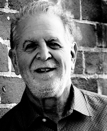 Rich Frank headshot wearing a collared shirt standing in front of a brick wall