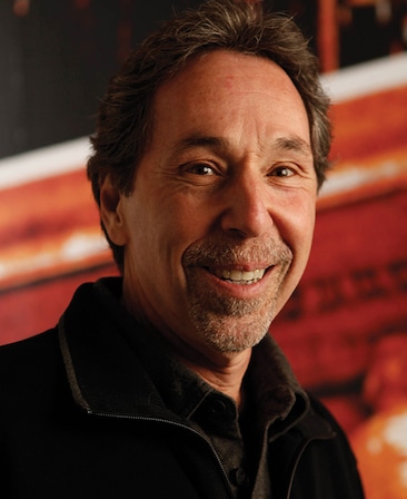 Mark Baker headshot in black jacket with red and white graphic image background