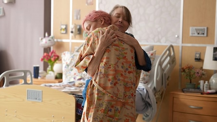 Molly with pink hair hugging her mom in a hospital room.