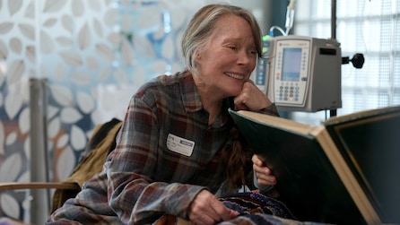 Gail sitting bedside in a hospital room and smiling. 