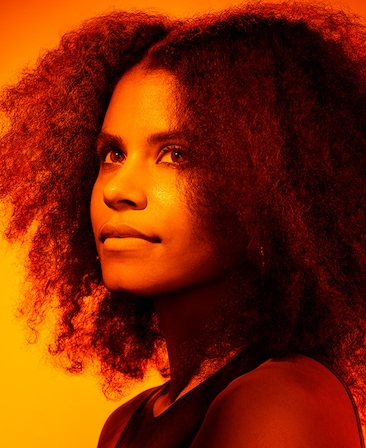 Headshot of Zazie Beetz in black shirt with heavy orange sunset lighting covering body and background