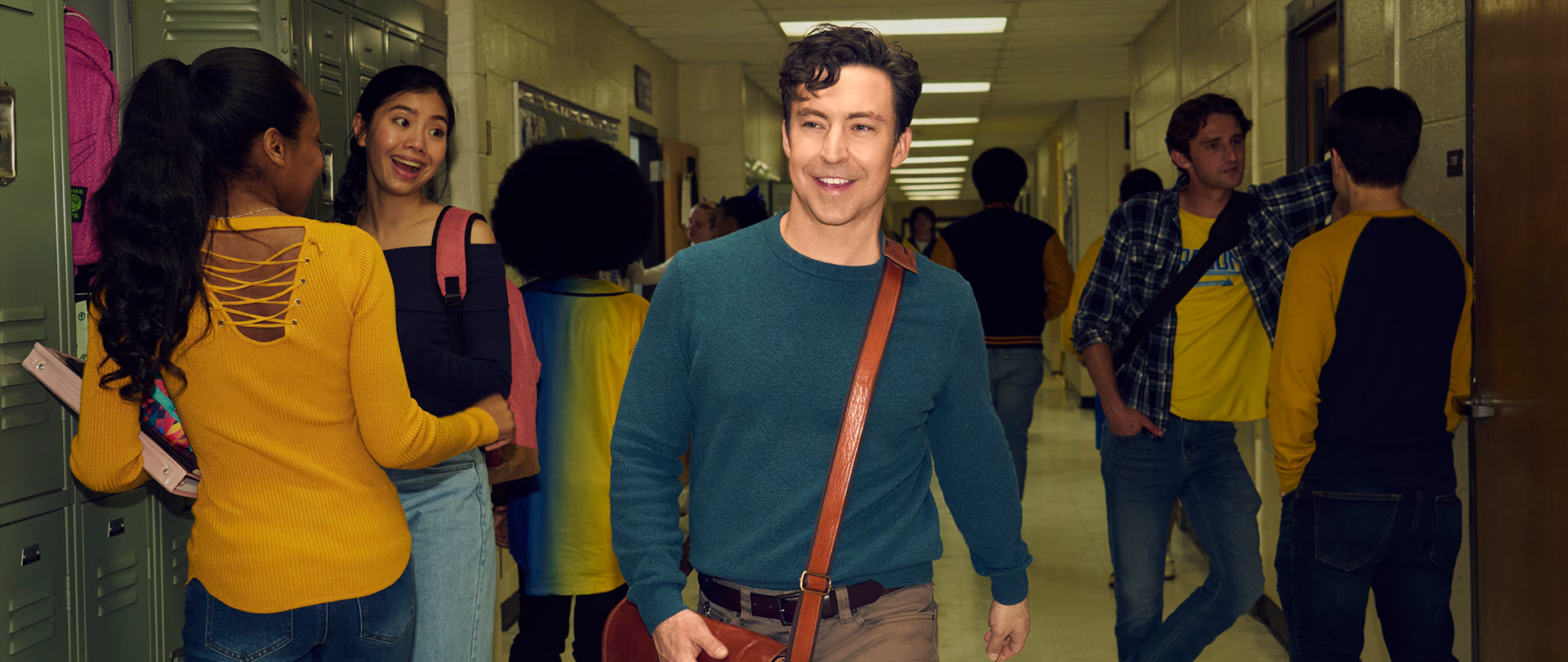 Teacher Evan wearing a dark blue sweater and a brown satchel.