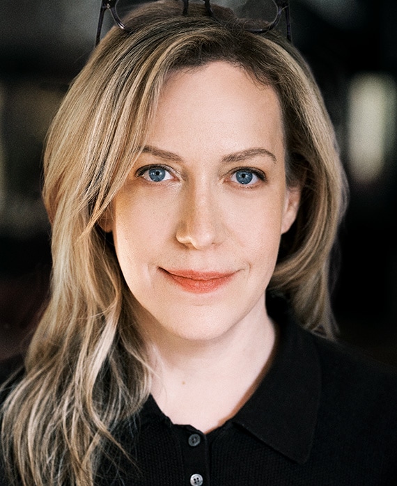Headshot of Kim Rosenstock wearing a black button up and glasses on top of her head.