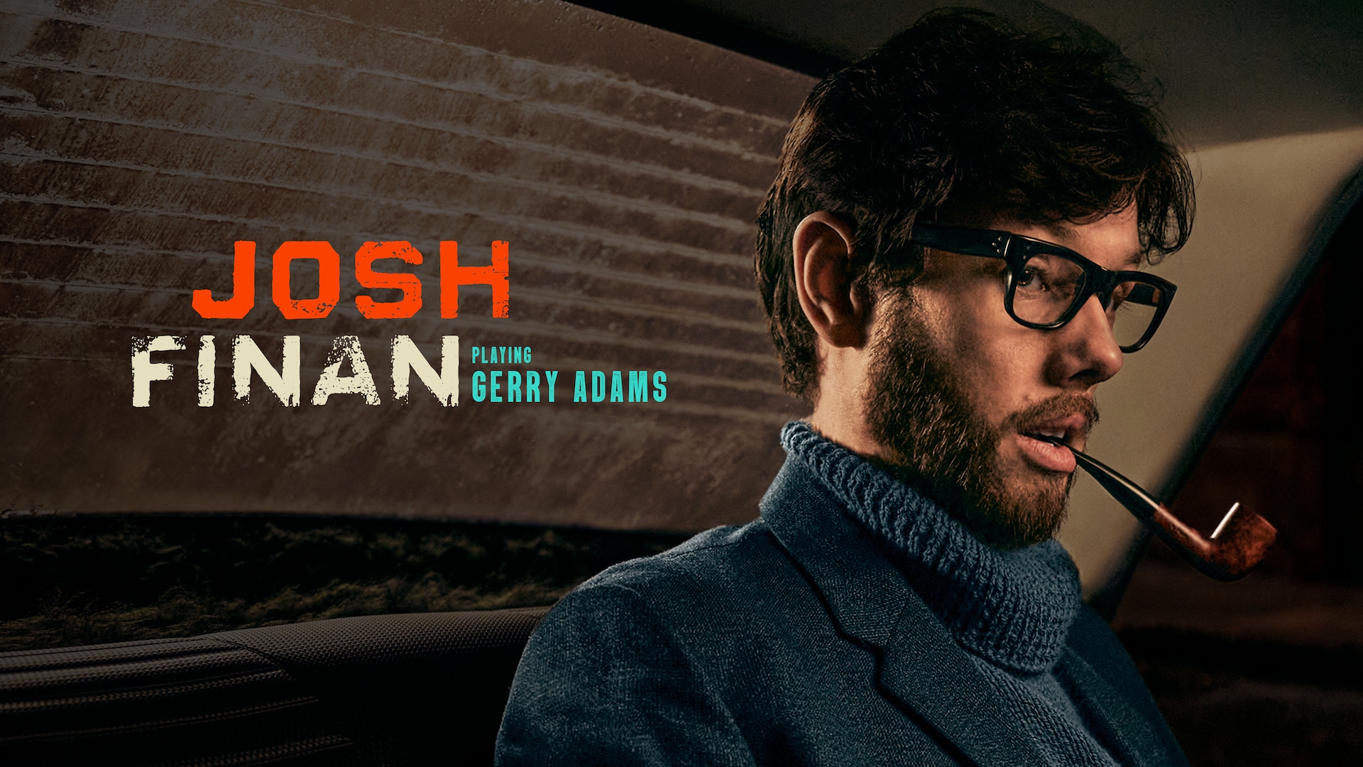 Josh Finan as Gerry Adams in FX's Say Nothing, wearing a blue sweater and black glasses with a brown pipe in his mouth.