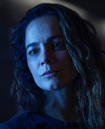 Alice Braga headshot standing in the dark wearing a black top