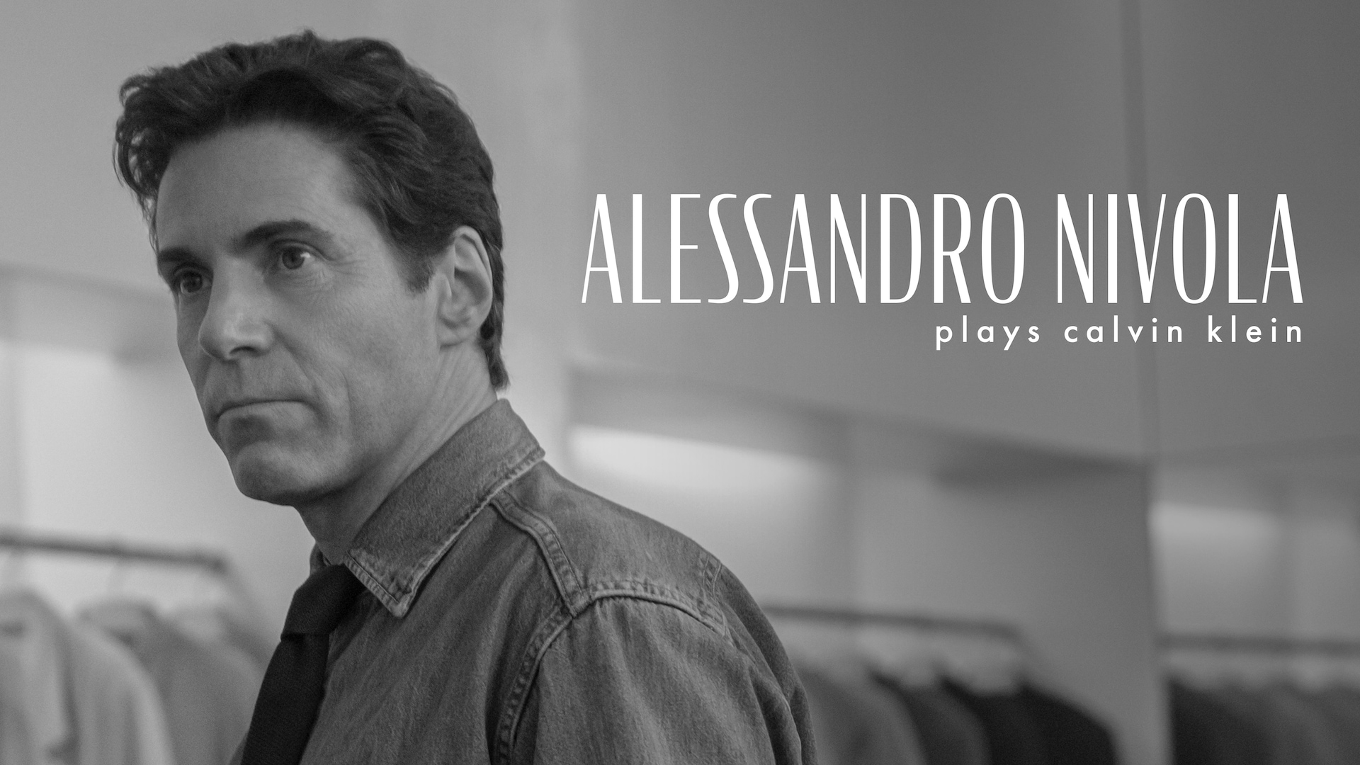 Black and white headshot of Alessandro Nivola as Calvin Klein in FX's Love Story wearing a denim jacket.