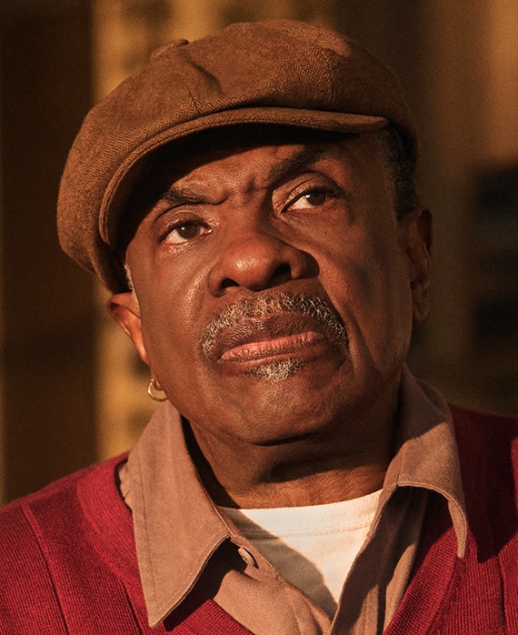 Headshot of Keith David as Marty in FX's The Lowdown, wearing a red and brown top, in a brown flat top hat.