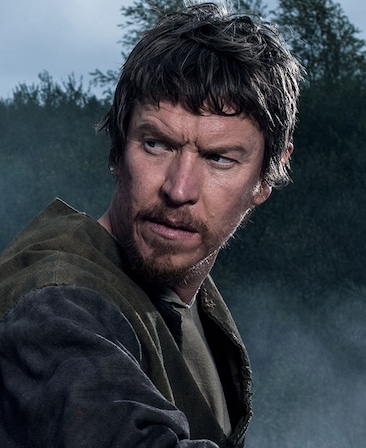 Sam Spruell headshot in textured olden peasant clothing with tall trees in background and covered by smoke