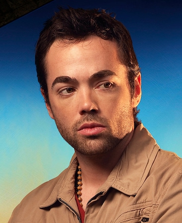 John Hensley headshot wearing a beaded necklace and beige jacket