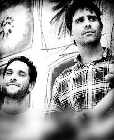 Reed Agnew and Eli Jorne's headshot standing next to each other wearing a plaid shirt and white t shirt