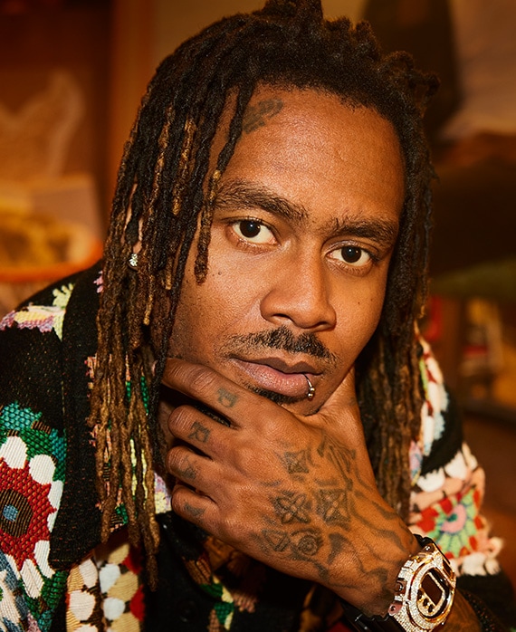 GaTa wearing a flower printed shirt and placing his hand on his chin